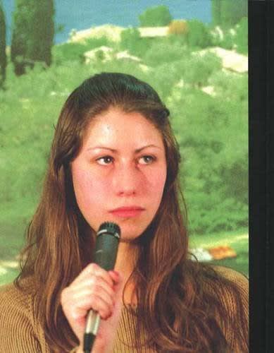Exhibition catalogue cover for Phil Collins exhibition "The World Won't Listen". A white young woman with long brown hair holds a microphone to face and stares.